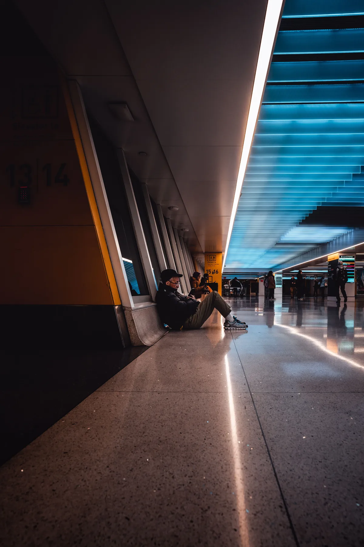 Travelers sitting on the floor of a long airport terminal corridor
