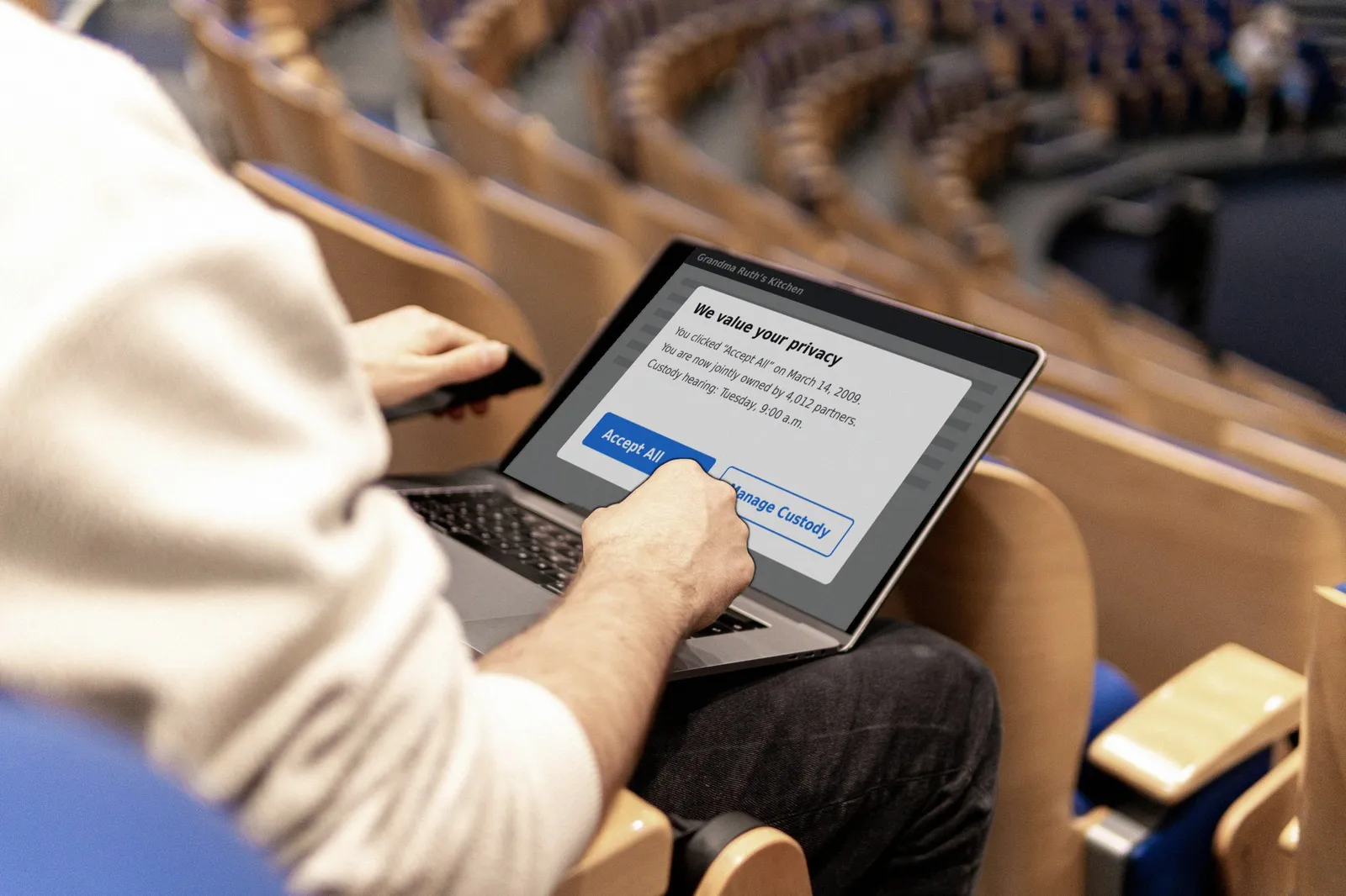 A man in an auditorium seat holds a laptop showing a cookie pop-up that says he is jointly owned by 4,012 partners, with buttons for Accept All and Manage Custody