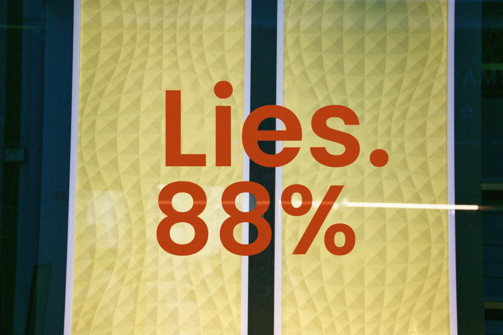 A shop window sign with large red letters on a yellow panel reading “Lies. 88%”