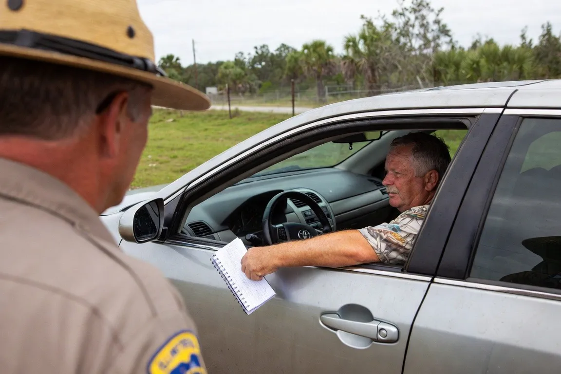 Florida state trooper looks on as a driver behind the wheel hands a spiral notebook out the window.