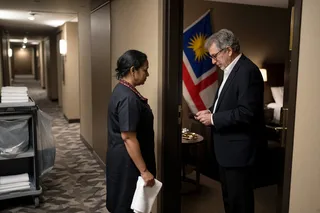 A hotel room door with a faded Do Not Disturb hanger, a handmade flag taped to the frame, an ‘Embassy of 412’ sign and yellow border tape across the hallway carpet