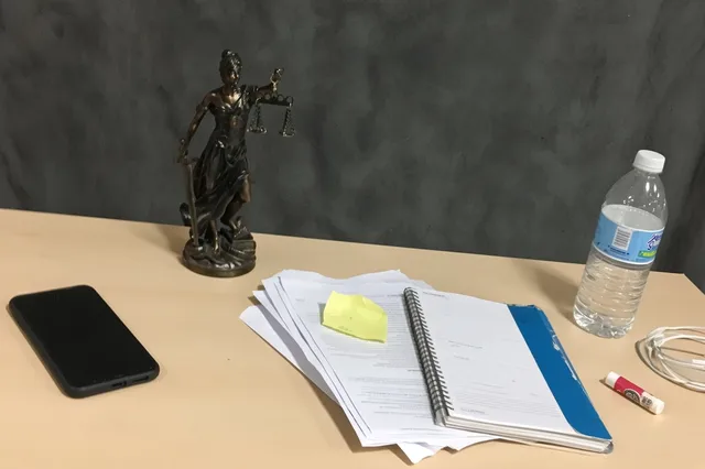 A bronze Lady Justice statue on a wooden desk beside a notebook, magnifying glass, and clipboard