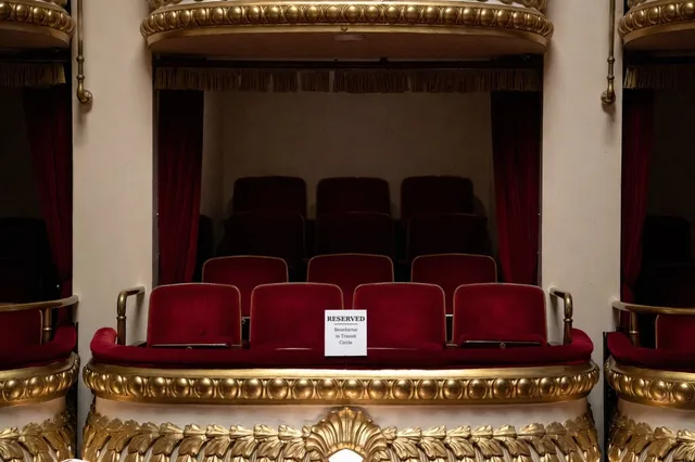 An empty private theater box with red velvet seats and a gold railing, with a small white card on the ledge reading Reserved, Benefactor in Transit Circle.