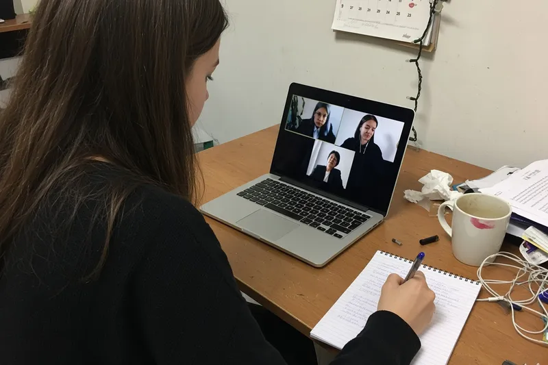 A woman at a desk on a video call with three colleagues on her laptop screen