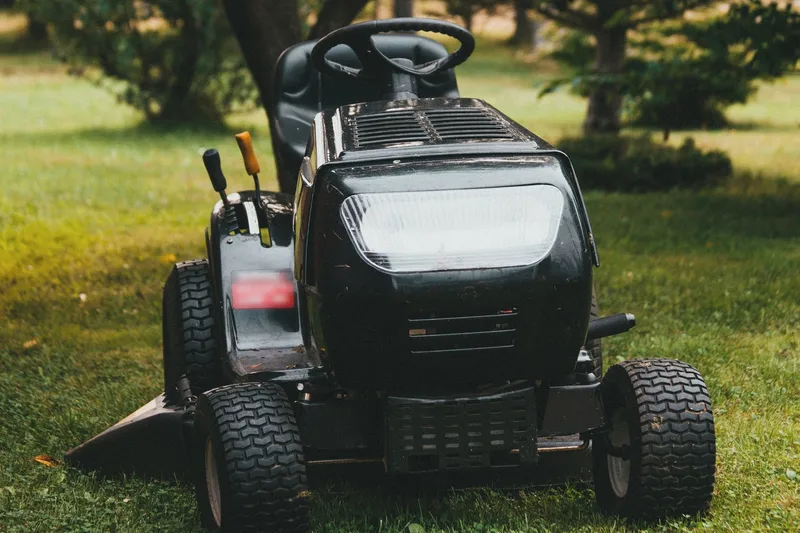 A black riding lawn mower parked on a grassy yard in front of leafy trees