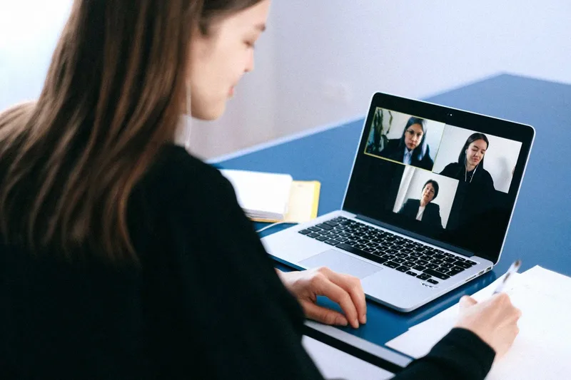 A woman at a desk on a video call with three colleagues on her laptop screen
