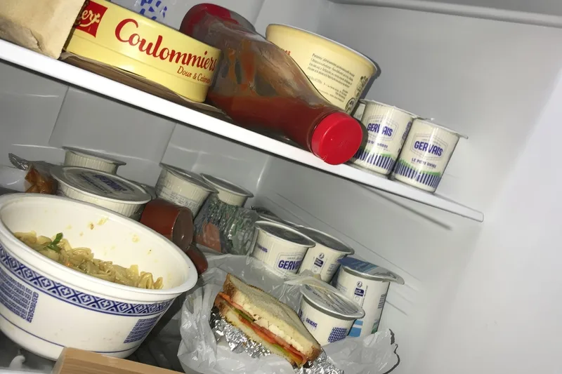 Rows of yogurt cups stacked on the shelves of a refrigerator next to a bowl and a tub of cheese.