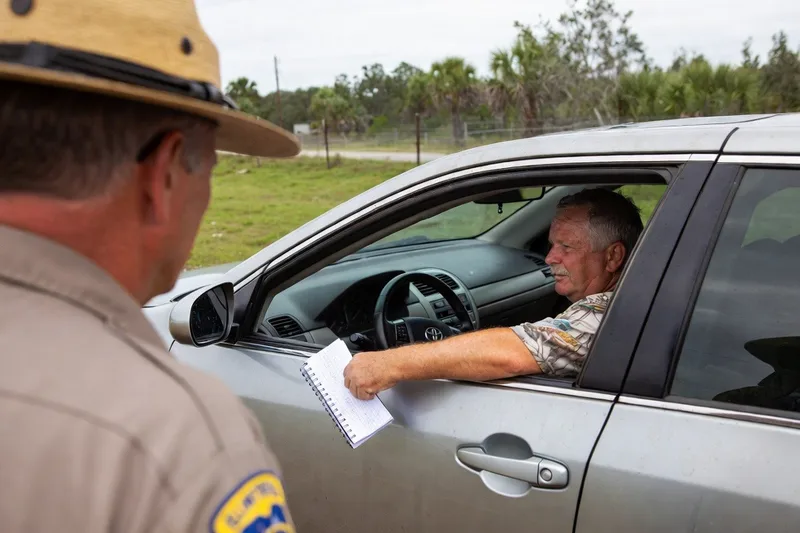 Florida state trooper looks on as a driver behind the wheel hands a spiral notebook out the window.